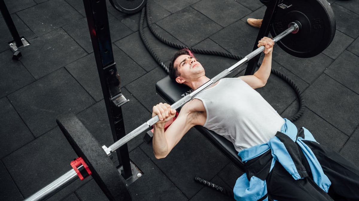 Adult male performing bench press in a Mexico City gym, showcasing strength training and fitness.